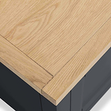 A light wooden tabletop at a corner joint, with visible grain, resting on a dark base or legs.