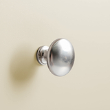 A round, metallic door knob is mounted on a cream-colored wall, reflecting light due to its polished surface.