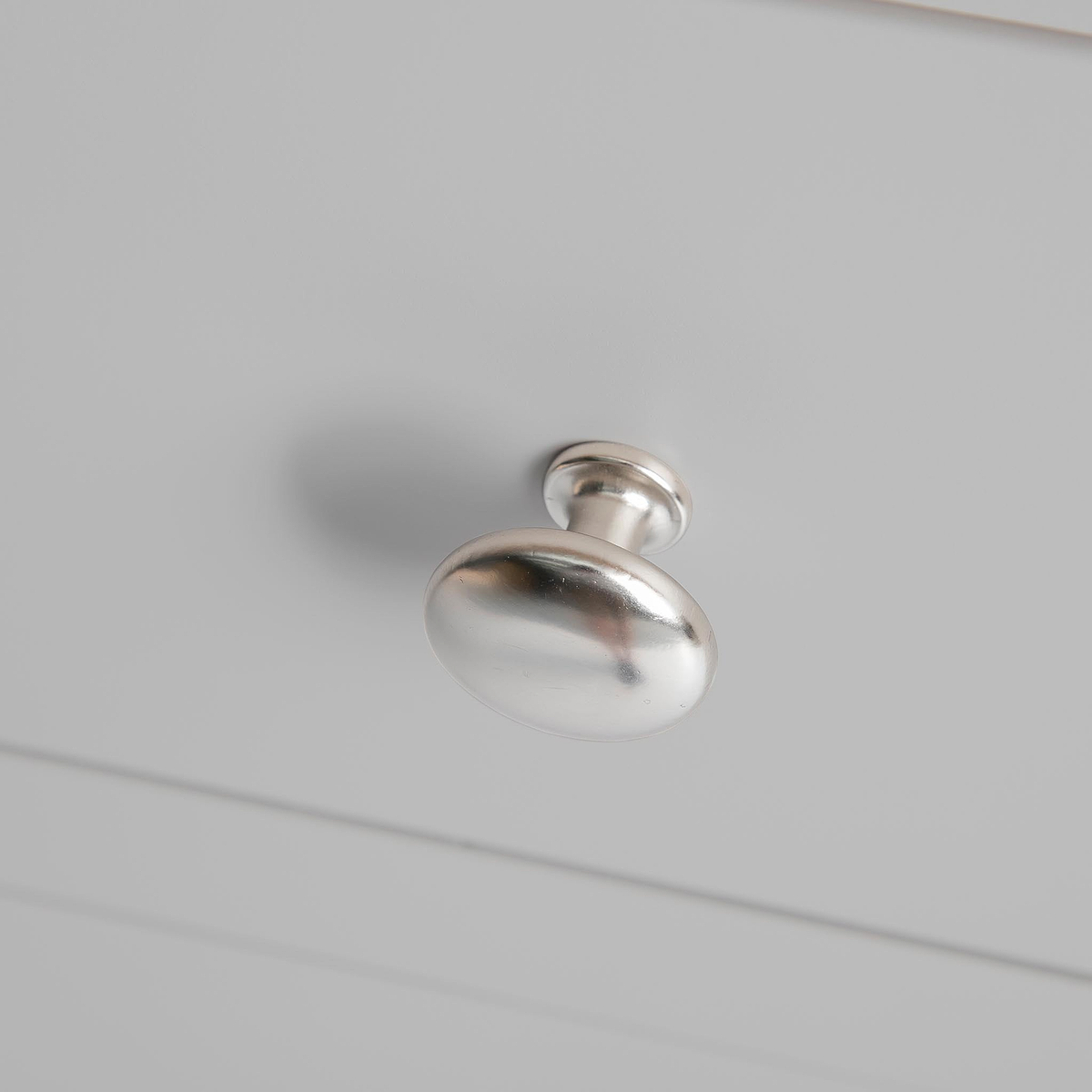 A silver drawer knob is mounted on a white panel, casting a soft shadow beneath it.
