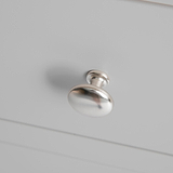 A silver drawer knob is mounted on a white panel, casting a soft shadow beneath it.