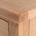 A close-up of a wooden table corner showing the texture and grain, with a blurred background emphasizing the woodworking detail.
