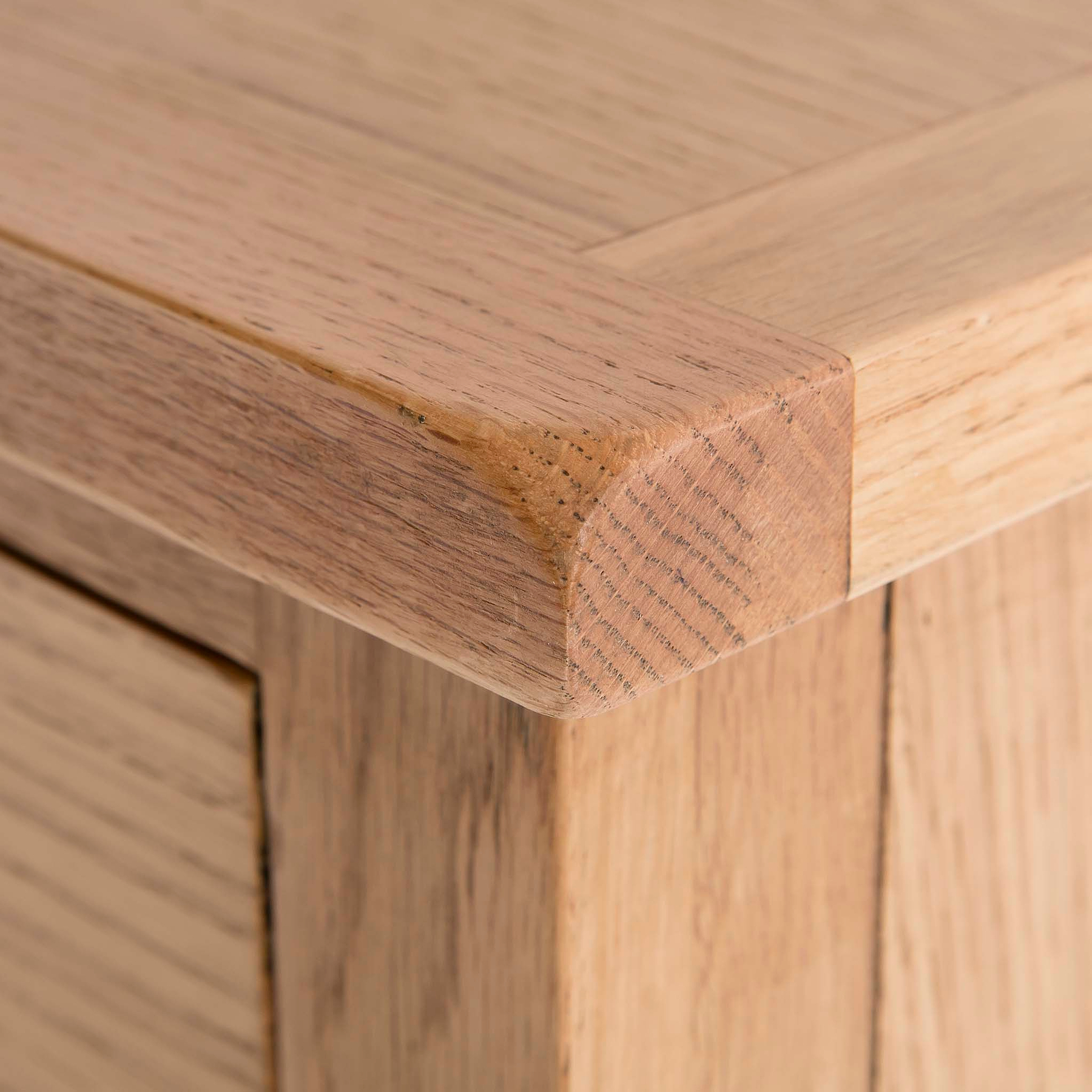 A close-up of a wooden table corner showing the texture and grain, with a blurred background emphasizing the woodworking detail.