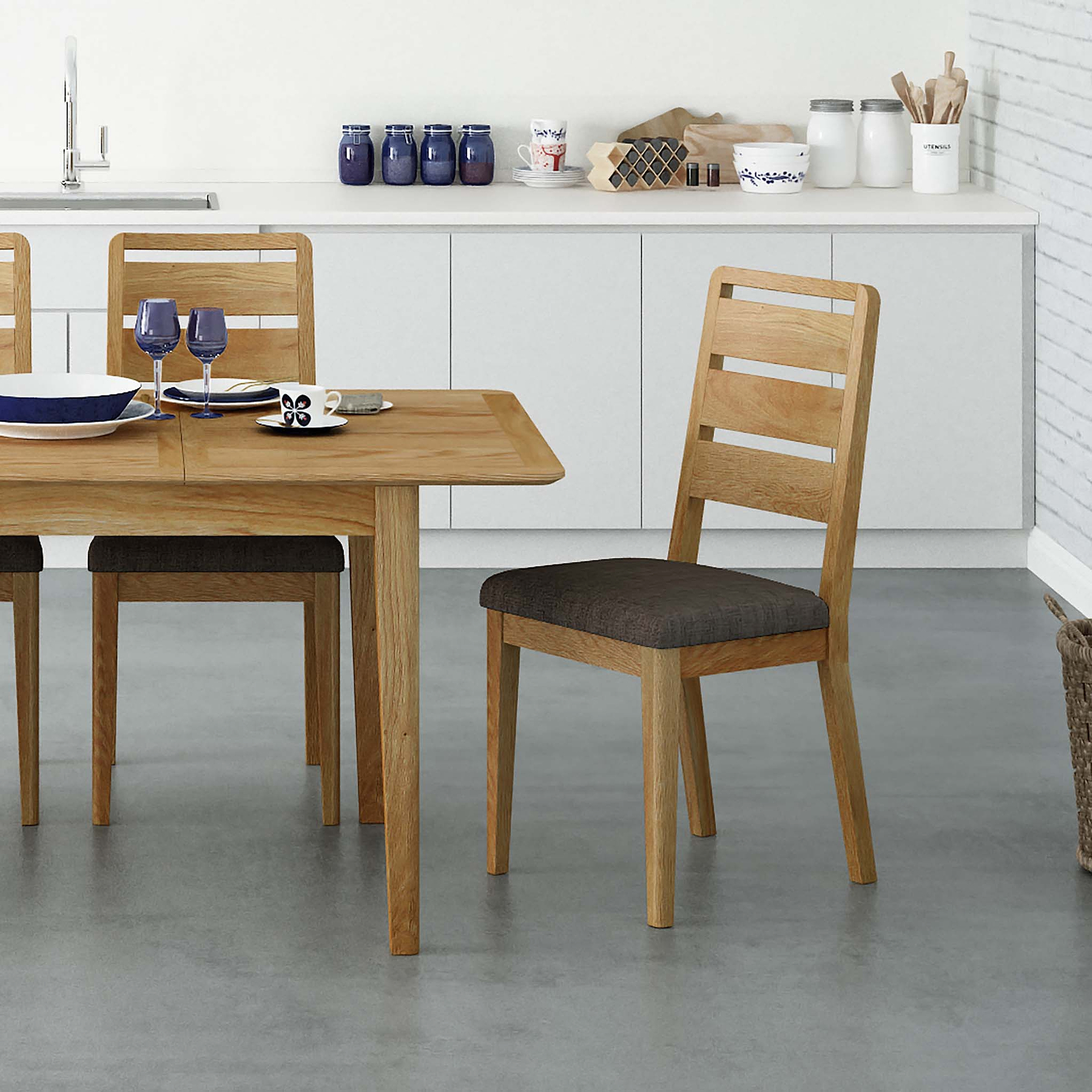 A wooden dining table with chairs, set with plates and glasses, in a modern kitchen with white cabinets and decorative items on the countertops.