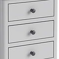 A white chest of drawers with three closed drawers, each featuring a round, black knob, set against a plain background.