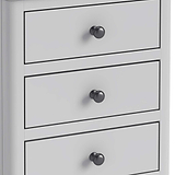 A white chest of drawers with three closed drawers, each featuring a round, black knob, set against a plain background.