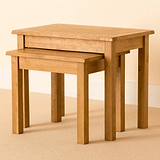 A pair of nested wooden tables, the smaller one partially slid beneath the larger, against a neutral-toned backdrop.