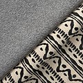 A gray textured blanket partially covers a patterned fabric with black and beige tribal designs, creating a cozy, home interior atmosphere.