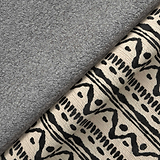 A gray textured blanket partially covers a patterned fabric with black and beige tribal designs, creating a cozy, home interior atmosphere.