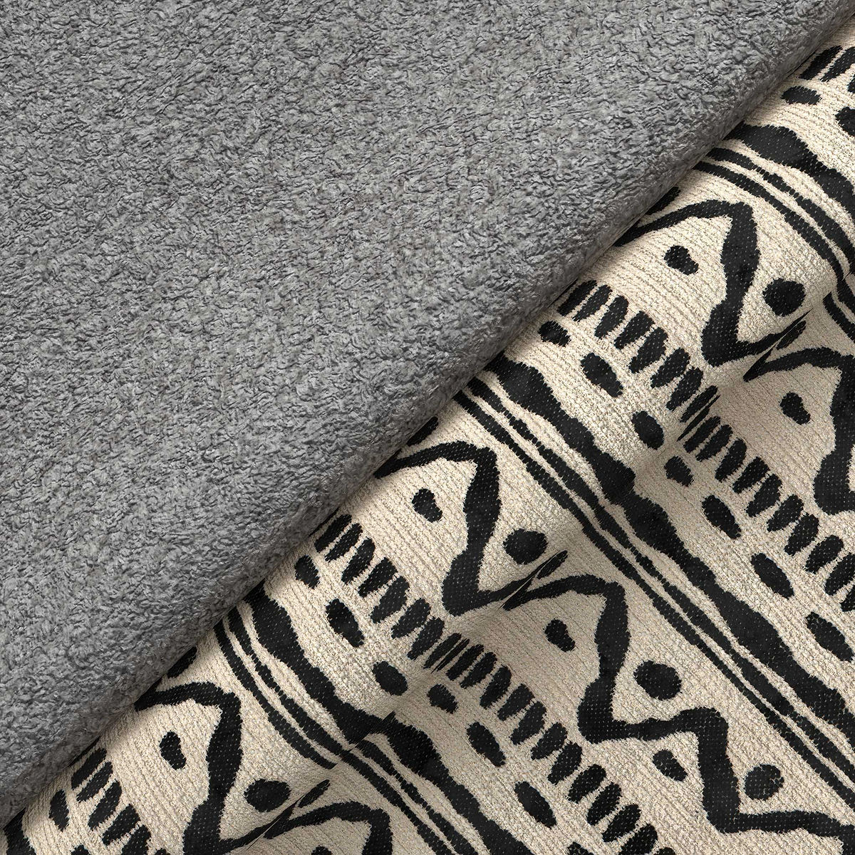 A folded gray fleece blanket rests atop a patterned fabric with black and beige tribal designs, suggesting a cozy, domestic setting.