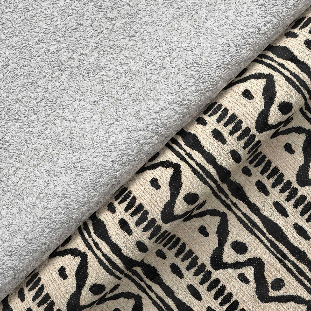 A gray plush towel rests on patterned fabric with abstract black designs, creating a contrast of textures.