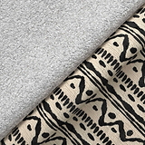 A gray plush towel rests on patterned fabric with abstract black designs, creating a contrast of textures.