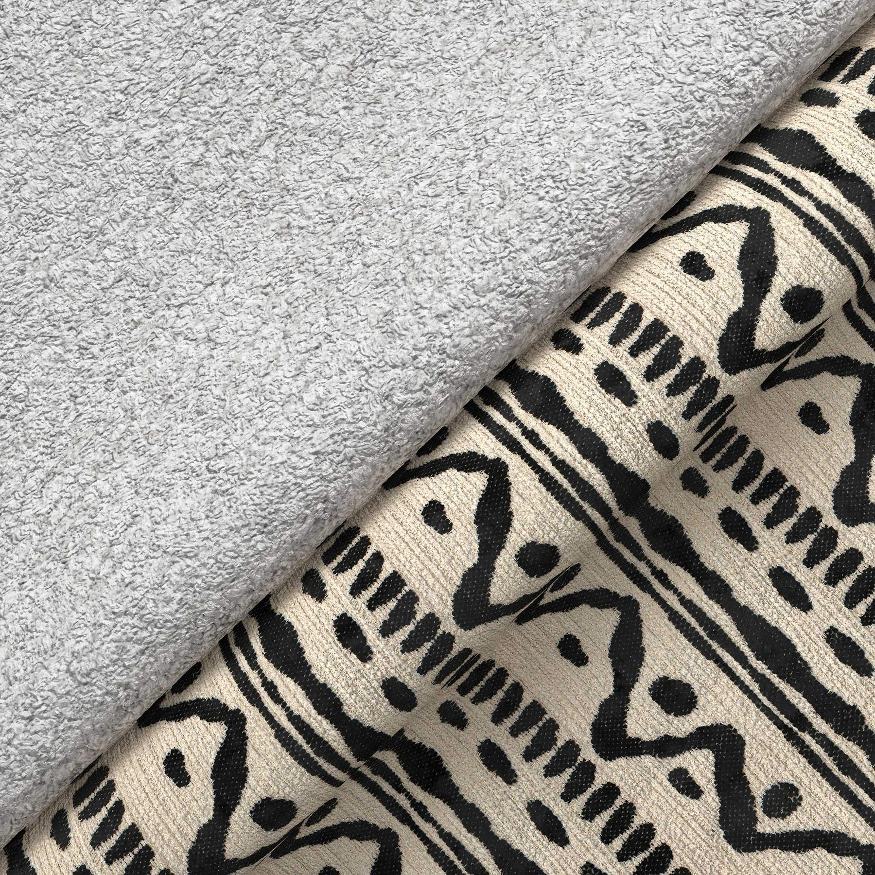 A gray plush towel rests on patterned fabric with abstract black designs, creating a contrast of textures.