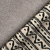 A gray fluffy towel rests on an intricately patterned fabric with black and beige designs, both textiles suggesting a cozy indoor setting.