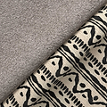 A grey fluffy towel overlaps a patterned fabric with geometric black designs on a beige background, suggesting a home decor setting.
