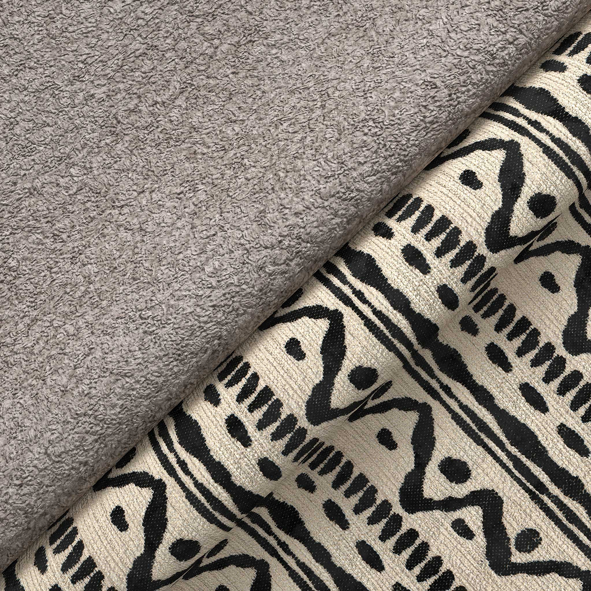 A grey fluffy towel overlaps a patterned fabric with geometric black designs on a beige background, suggesting a home decor setting.