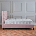 A pink, tufted single bed against a grey paneled wall, on a herringbone patterned wooden floor.