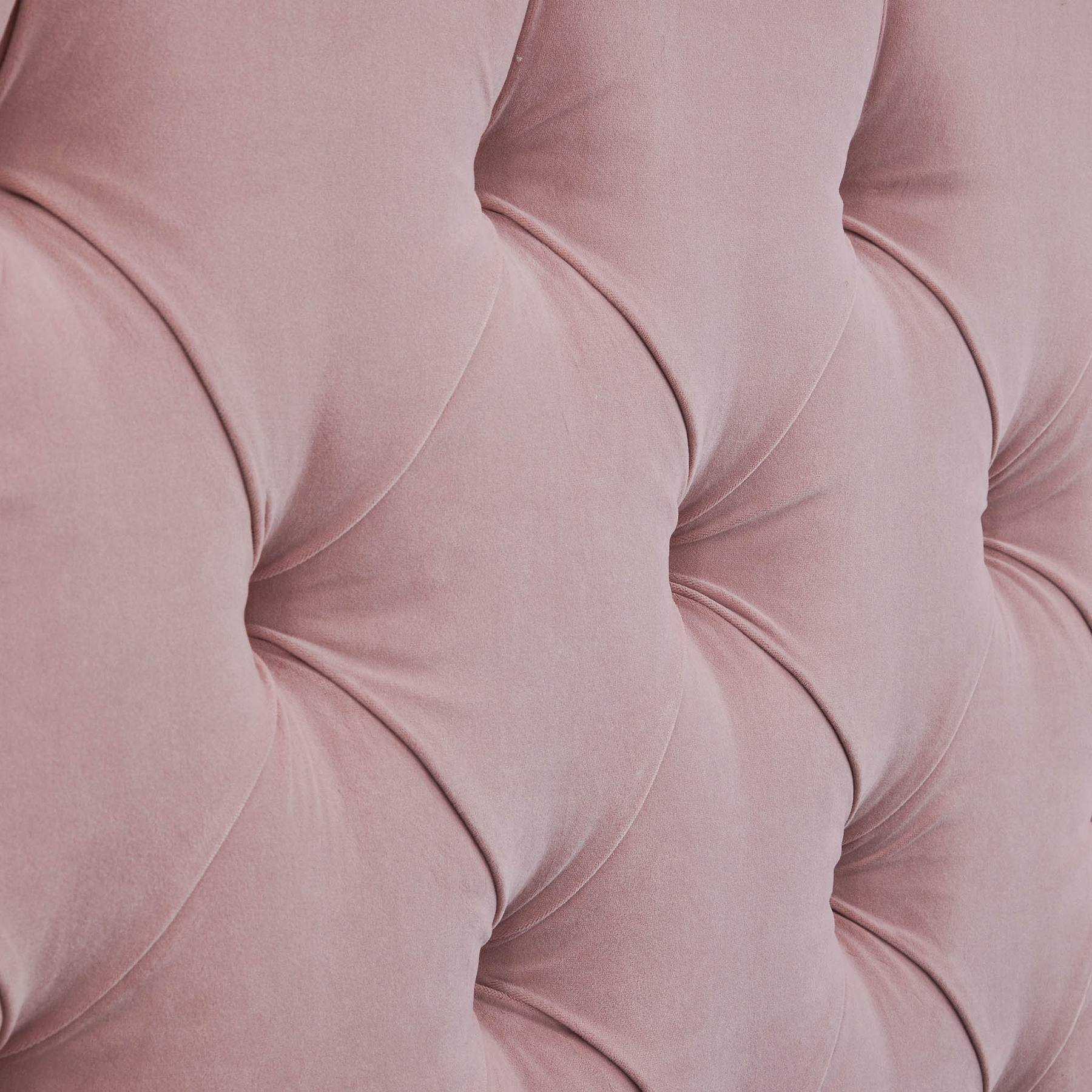 A close-up of a pink, tufted fabric forming a diamond pattern with visible stitching and shadows accentuating its plush texture.