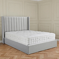 A grey upholstered bed with a plush mattress in an elegant room with paneled walls and herringbone wood flooring.