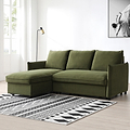 A green sectional sofa with chaise lounge sits on a patterned rug, under a floor lamp, beside a large window, with an art frame on the wall.