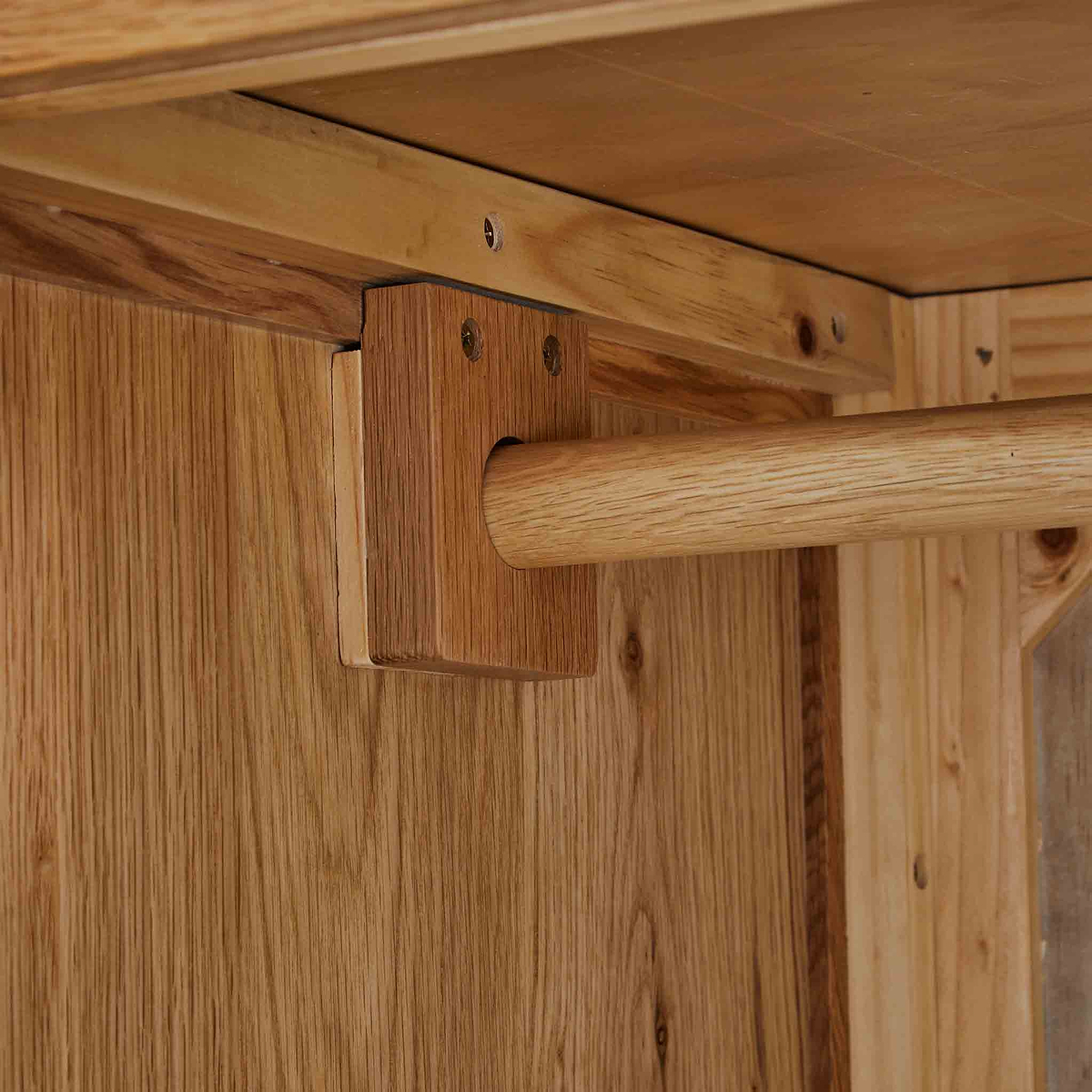 A wooden dowel passes through a bracket, securing it against a vertical wooden surface, likely part of a furniture assembly.