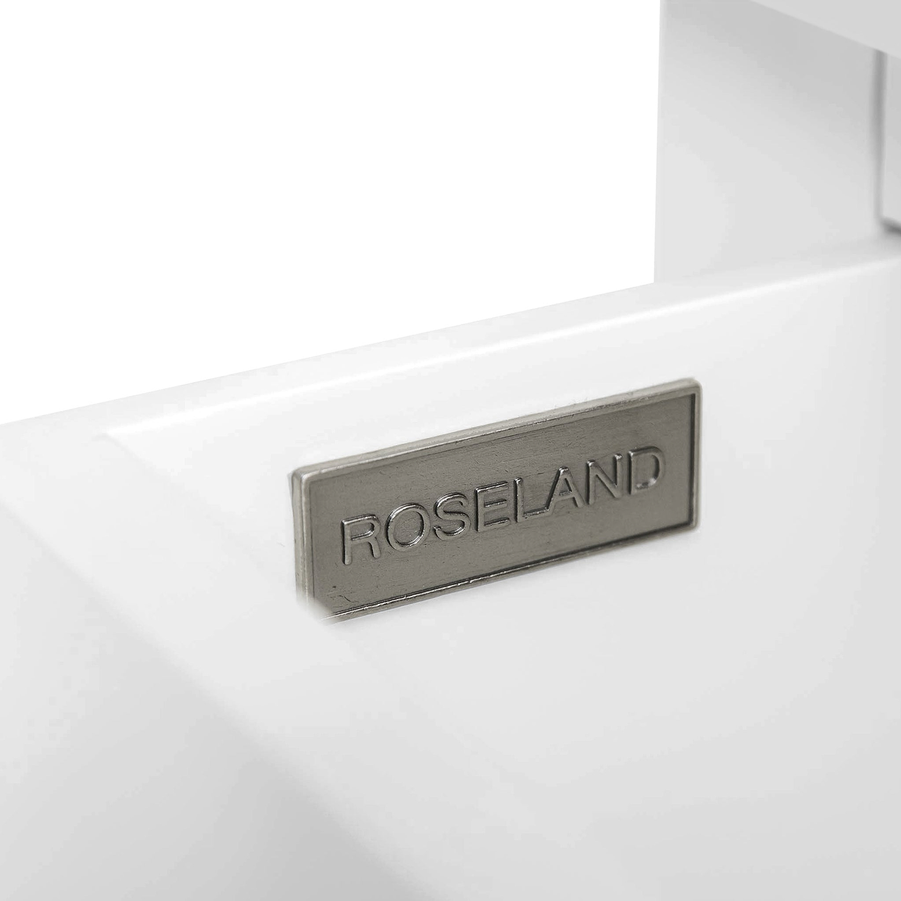 A metal plate with the inscription "ROSELAND" is affixed to a white surface, set against a plain background.