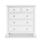 A white wooden chest of drawers with silver knobs stands against a plain background; two small upper drawers flank a third, above three larger drawers.