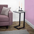 A side table with a mug and candles resting on it, situated next to a pink armchair, against a white and purple wall, above a grey carpet.