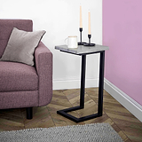 A side table with a mug and candles resting on it, situated next to a pink armchair, against a white and purple wall, above a grey carpet.