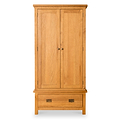 A wooden wardrobe stands closed against a white background, with one drawer at the bottom, and two round handles on the doors.