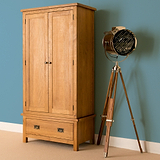 A wooden armoire stands next to a tripod-based spotlight lamp against a teal wall on a beige carpet.