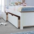 A white children's bed with storage drawers underneath sits adorned with pillows and stuffed toys, in a tidy, bright room with a toy car on the floor.