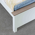 A partially visible cream-colored mattress rests on a white bed frame with a wooden slat, set against a grey carpeted floor.