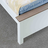 A partially visible cream-colored mattress rests on a white bed frame with a wooden slat, set against a grey carpeted floor.