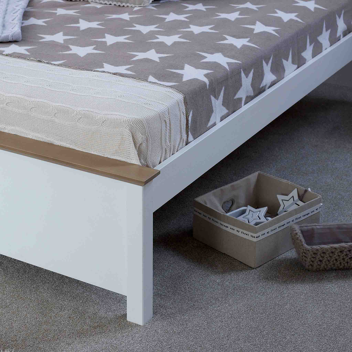 A neatly-made bed with a star-patterned blanket and a knitted throw at the foot, situated in a tidy room. A cardboard storage box rests on the floor by the bed.