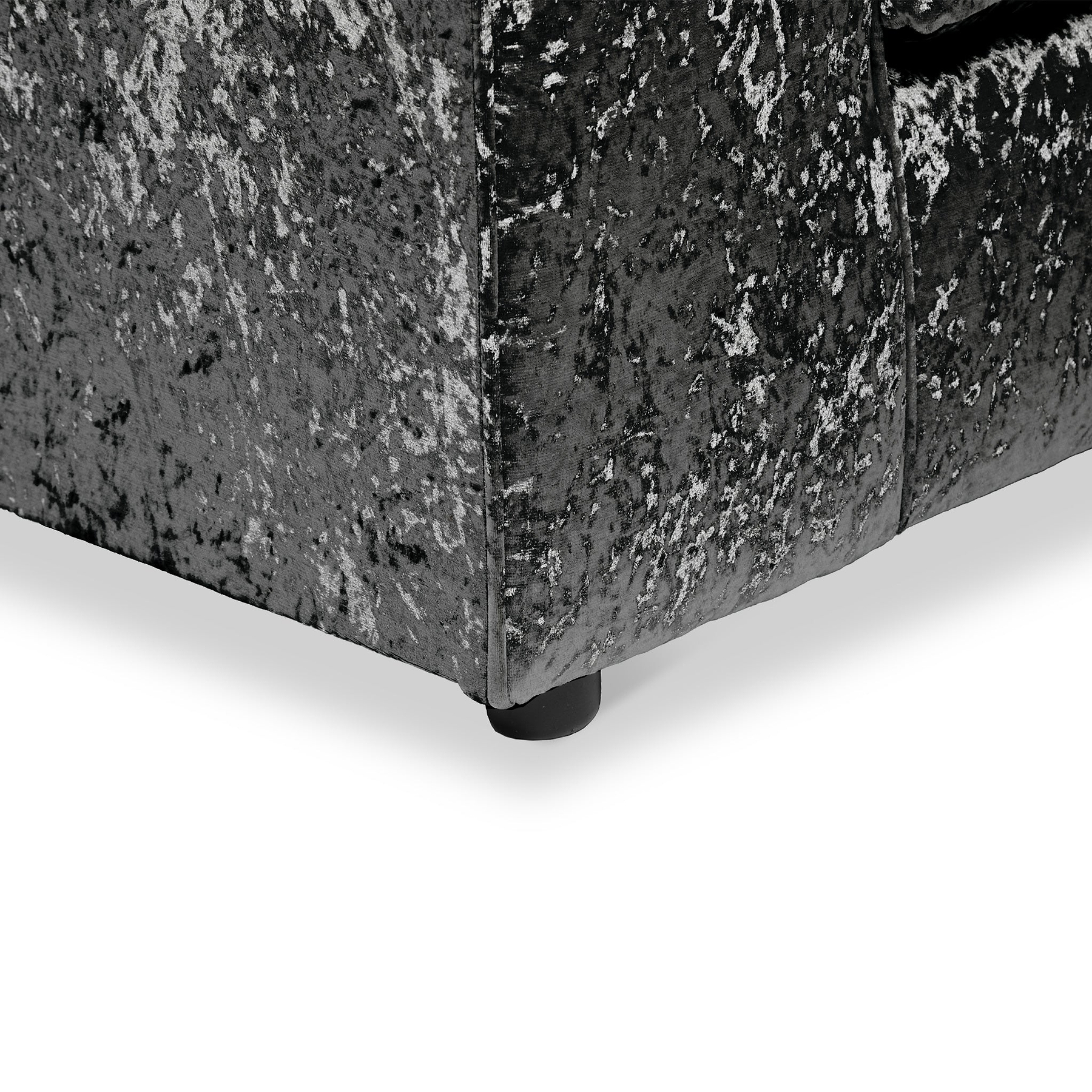 A corner of a gray patterned upholstered ottoman with a visible round black leg on a light background.