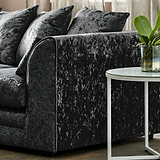 A crushed velvet sofa with plush pillows near a marble-topped side table with a plant, set against a curtained window.