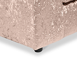 A portion of a light pink, plush-textured sofa with visible corner and black round leg set against a plain white background.