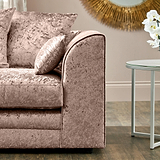 Velvet-textured, plush mauve sofa with matching pillows is resting, situated in a well-lit room with minimalistic decor, including a white side table and ornamental wall art.