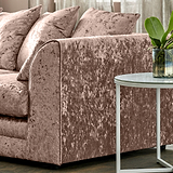 A plush, pink crushed velvet sofa with many matching pillows; a round white marble side table holds a potted plant, situated in a cozy living room.
