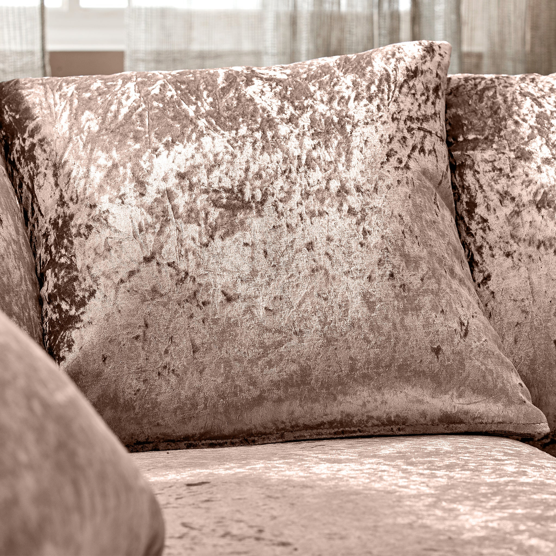 Two plush velvet pillows resting against each other on a sofa, bathed in soft natural light filtering through a window, imparting a cozy, serene ambiance.