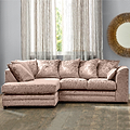 A plush L-shaped pink sectional sofa is positioned in a room with sheer curtains, wooden flooring, and a decorative mirror on the wall.