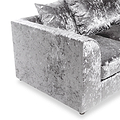 A velvet-textured sofa with plush cushions, in a neutral color, rests against an isolated white background.
