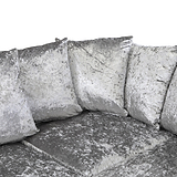 Four silver velvet cushions rest against each other on a matching couch, isolated against a white background.