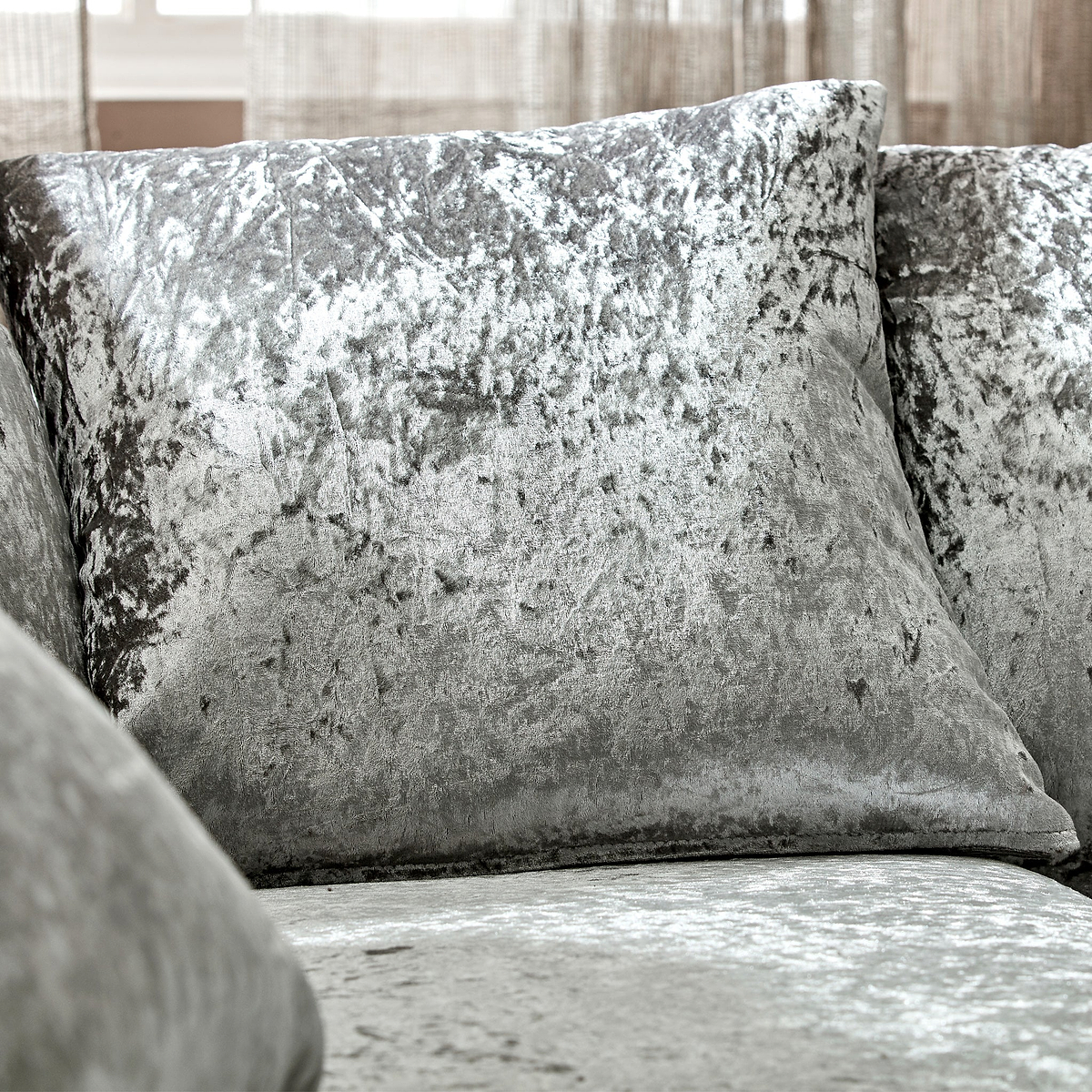 Velvet cushions rest on a sofa, creating a cozy indoor setting with a sheer curtained window in the background.