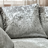 Velvet cushions rest on a sofa, creating a cozy indoor setting with a sheer curtained window in the background.