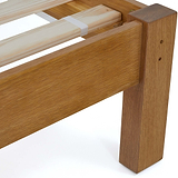 A wooden bed frame corner, with visible slats and support straps, against a white background.