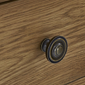 A round, antique-style drawer knob is affixed to a wooden surface with visible grain pattern, suggesting a furniture setting.