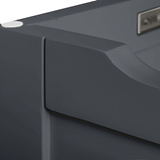 A close-up of a smooth dark gray surface with a curved edge and a metallic logo, possibly part of electronic equipment or furniture, against a blurred background.