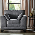 A charcoal gray armchair with two matching pillows is positioned near a round side table with decorative items, against a window with sheer curtains and a tree outside.