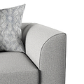 A patterned pillow rests against the curved, grey upholstered arm of a sofa, depicting a close-up of comfortable home furniture.